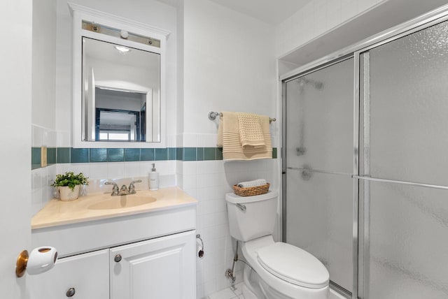 bathroom with tile walls, a shower stall, vanity, toilet, and a wainscoted wall