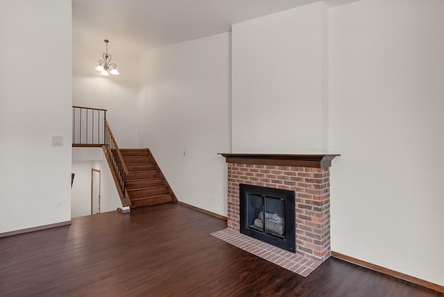unfurnished living room with wood finished floors, stairs, a fireplace, a chandelier, and baseboards