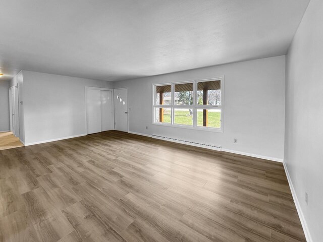 4538 Oakdale Dr, Racine, WI 53405 - unfurnished living room featuring a baseboard heating unit, wood finished floors, and baseboards
