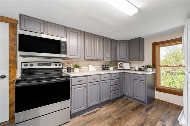 kitchen with appliances with stainless steel finishes, gray cabinets, wood finished floors, light countertops, and baseboards