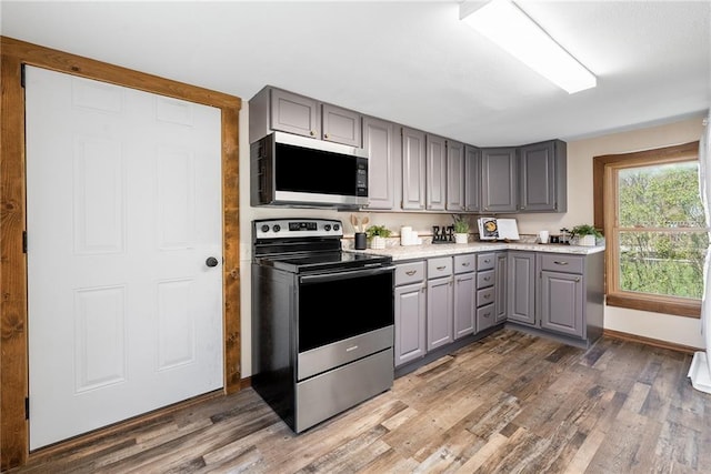 kitchen with appliances with stainless steel finishes, gray cabinetry, wood finished floors, and light countertops