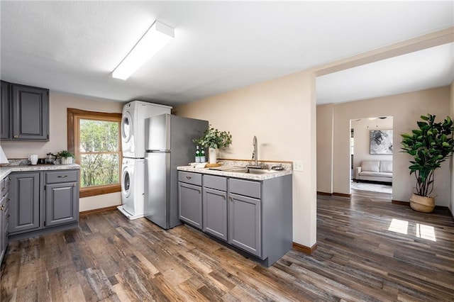 kitchen with gray cabinets, freestanding refrigerator, estacked washer and dryer, a sink, and dark wood-type flooring