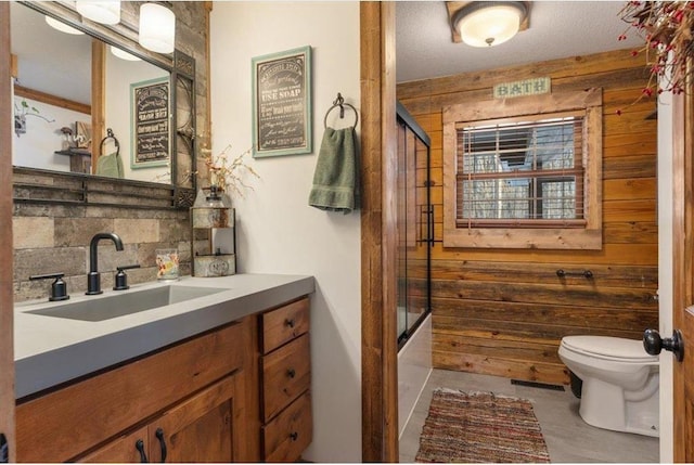 744 50th Ave, Clear Lake, WI 54005 - bathroom with wood walls, decorative backsplash, toilet, vanity, and shower / bath combination with glass door