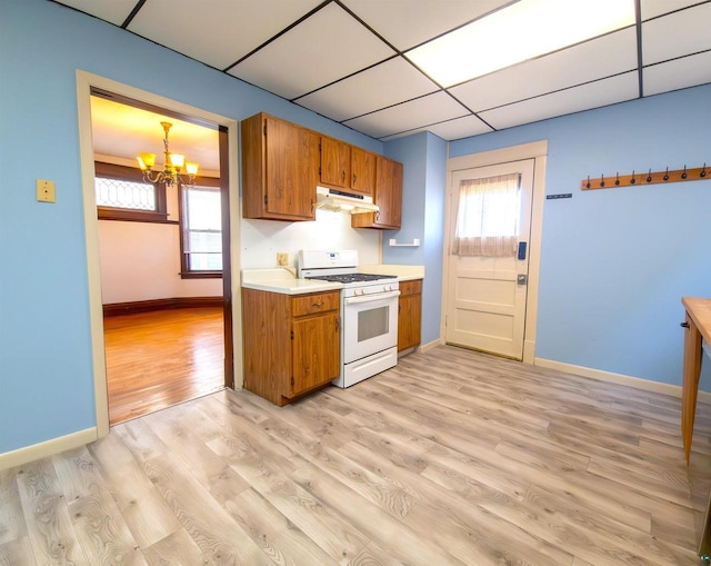 kitchen with white gas range oven, under cabinet range hood, a chandelier, brown cabinetry, and light countertops