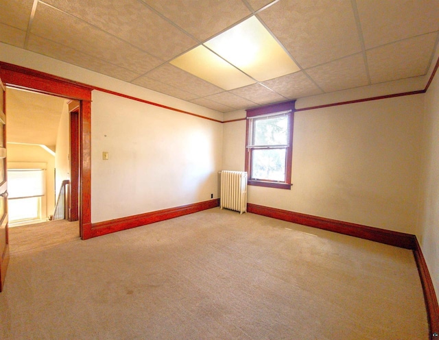 empty room featuring radiator heating unit, carpet floors, baseboards, and a drop ceiling