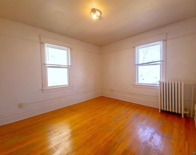 unfurnished room with radiator, light wood-style flooring, healthy amount of natural light, and baseboards
