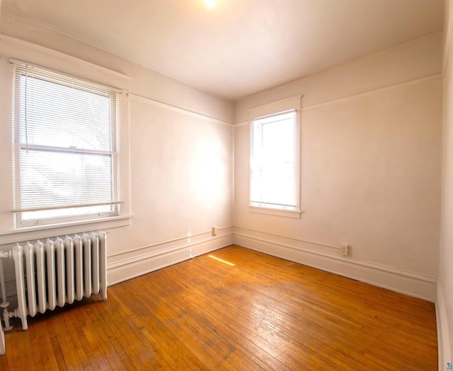 unfurnished room with radiator heating unit, hardwood / wood-style floors, and baseboards