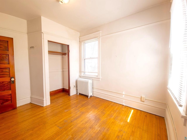 unfurnished bedroom with radiator, light wood-type flooring, a closet, and baseboards
