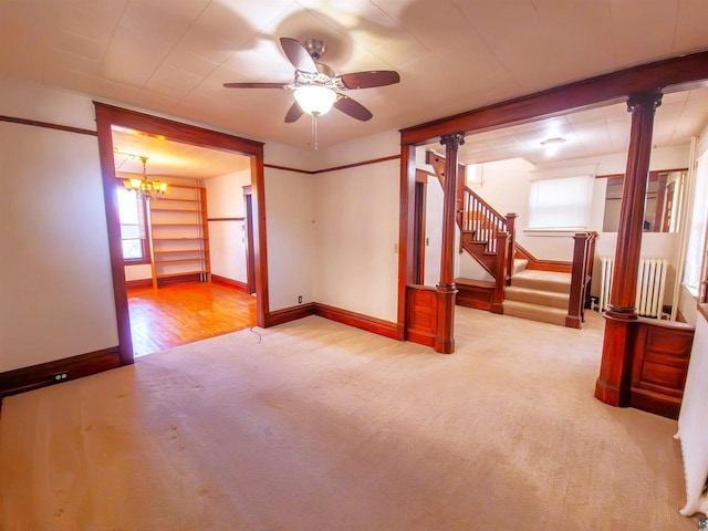 carpeted spare room with baseboards, ceiling fan, stairs, ornate columns, and a chandelier
