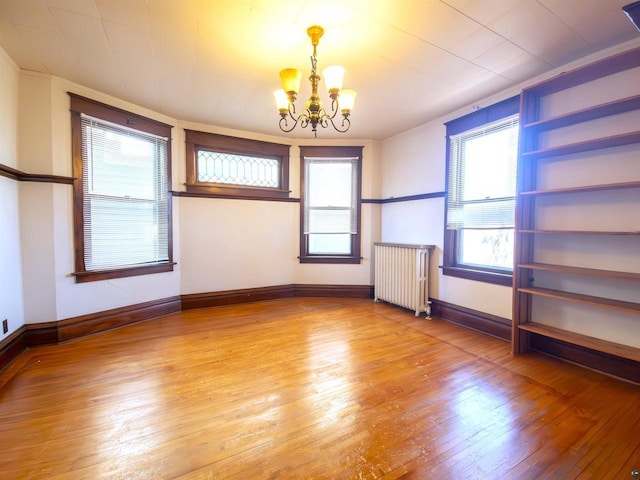 unfurnished room with radiator, a chandelier, hardwood / wood-style floors, and baseboards