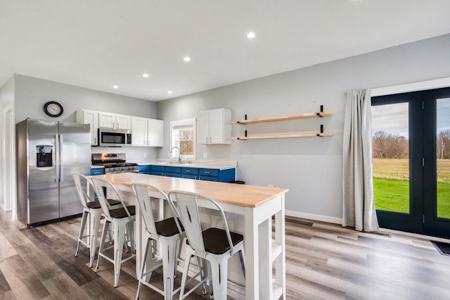 2965 S Stevenson Pier Rd, Sturgeon Bay, WI 54204 - kitchen with appliances with stainless steel finishes, blue cabinetry, a sink, open shelves, and wood finished floors