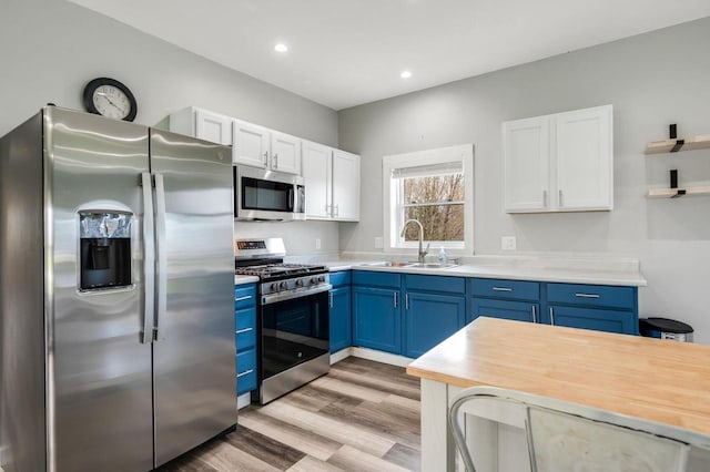 2965 S Stevenson Pier Rd, Sturgeon Bay, WI 54204 - kitchen with stainless steel appliances, blue cabinets, a sink, light wood-style flooring, and white cabinetry