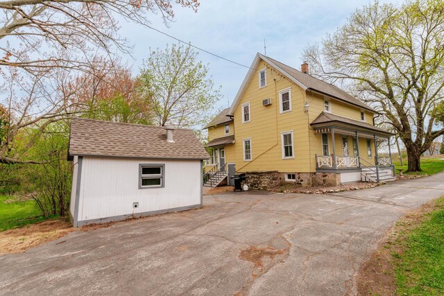 12220 W Highland Rd, Mequon, WI 53097 - view of home's exterior with covered porch, an outbuilding, a shingled roof, driveway, and a chimney