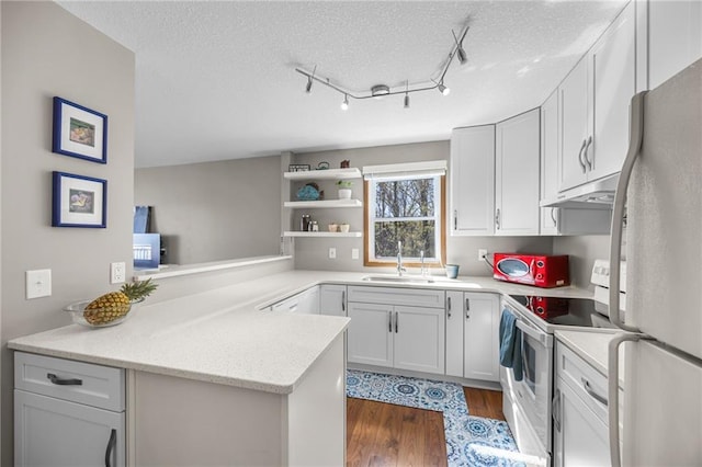 1141 134th Ave, Amery, WI 54001 - kitchen with white appliances, under cabinet range hood, a sink, dark wood-style floors, and a peninsula