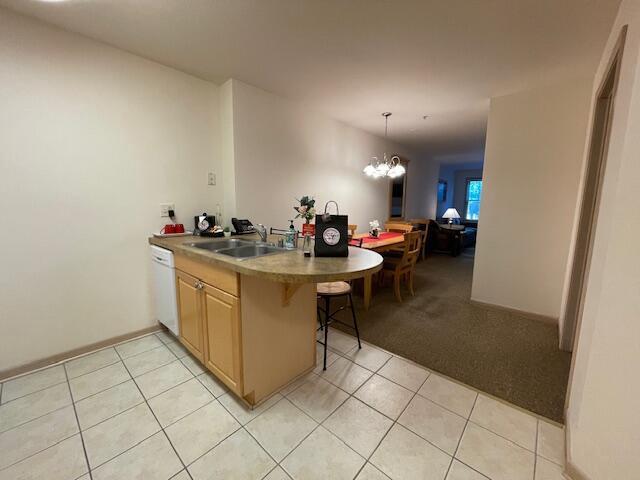 123 Center St Unit 101, Lake Geneva, WI 53147 - kitchen featuring a sink, white dishwasher, a peninsula, a chandelier, and light tile patterned flooring