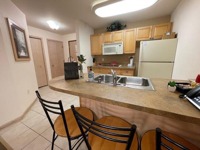123 Center St Unit 101, Lake Geneva, WI 53147 - kitchen featuring white appliances, light brown cabinets, a kitchen bar, a sink, and light tile patterned floors