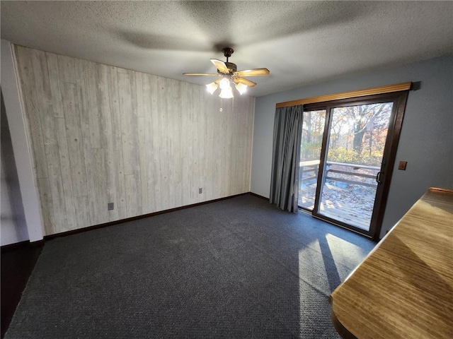 1451 90th Ave, Amery, WI 54001 - spare room featuring wooden walls, ceiling fan, dark carpet, a textured ceiling, and baseboards