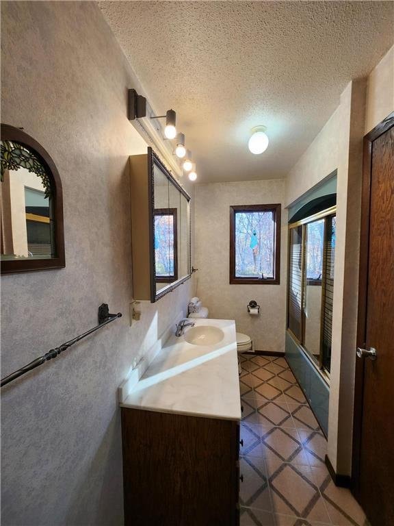 1451 90th Ave, Amery, WI 54001 - bathroom with toilet, a textured ceiling, vanity, bath / shower combo with glass door, and tile patterned flooring