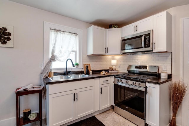 932 Washburn St, Beloit, WI 53511 - kitchen with appliances with stainless steel finishes, a sink, dark countertops, white cabinetry, and decorative backsplash