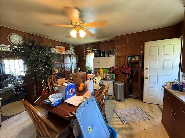 dining area featuring a ceiling fan, wood walls, and light colored carpet