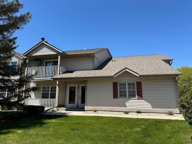 view of front of property featuring a balcony, a shingled roof, and a front yard