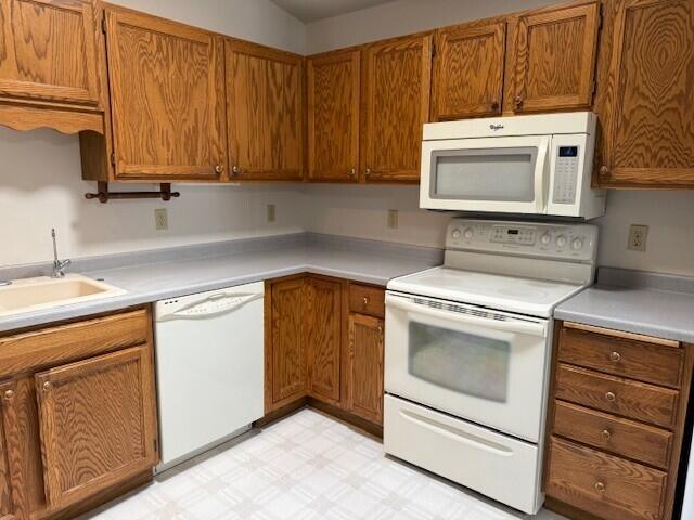 kitchen with white appliances, light flooring, brown cabinets, a sink, and light countertops