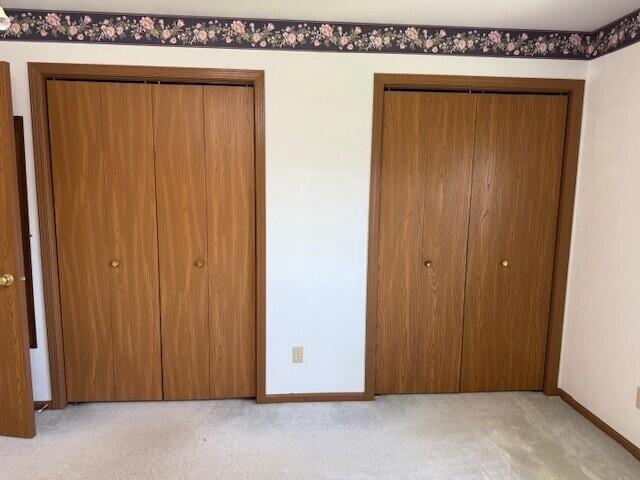 unfurnished bedroom with light carpet, baseboards, and multiple closets