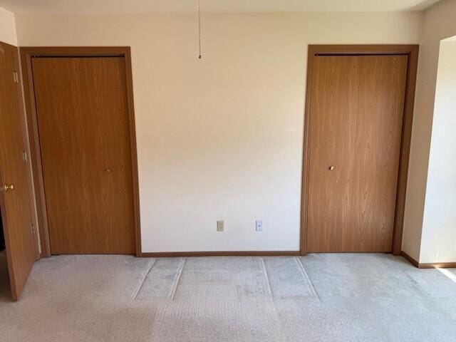 unfurnished bedroom with light carpet, baseboards, and multiple closets