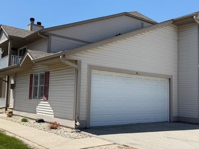 view of side of home with an attached garage, a chimney, and driveway
