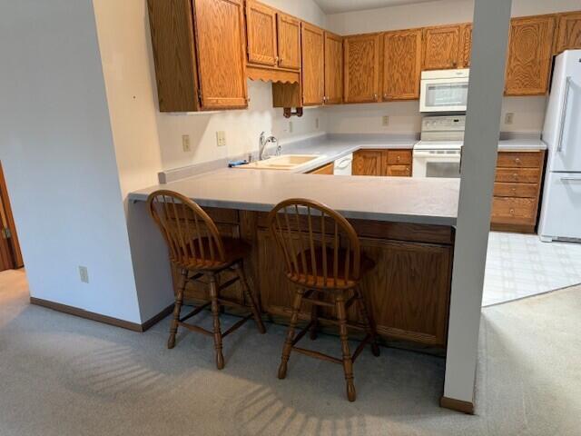 kitchen with white appliances, a sink, light carpet, light countertops, and a peninsula