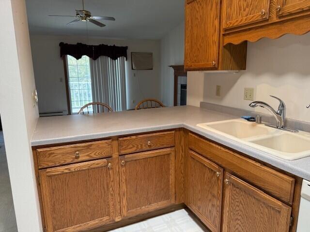 kitchen featuring a sink, ceiling fan, baseboard heating, brown cabinetry, and light countertops