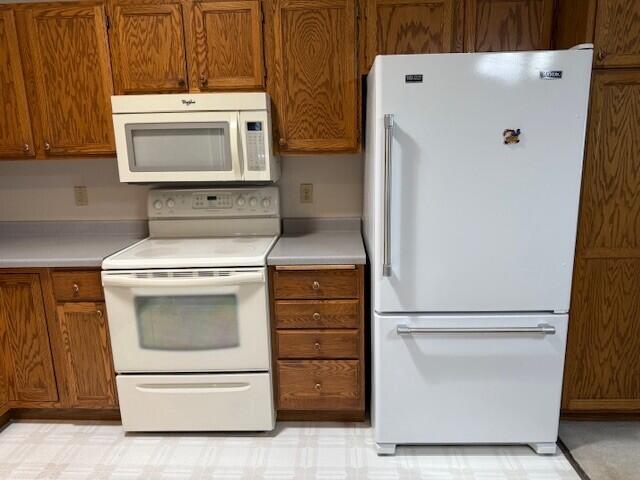kitchen featuring white appliances, brown cabinetry, and light countertops