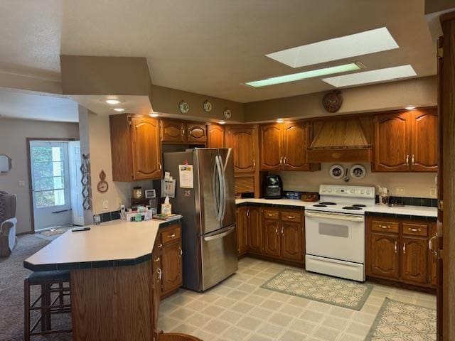 N115W21032 Brookside Cir, Germantown, WI 53022 - kitchen featuring white electric range, freestanding refrigerator, a peninsula, a skylight, and a kitchen breakfast bar