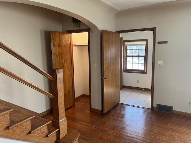 interior space featuring wood finished floors, stairs, arched walkways, baseboards, and ornamental molding