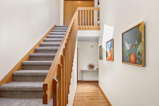 staircase featuring wood finished floors, baseboards, and a towering ceiling