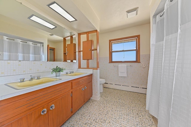 full bath with a baseboard radiator, tile walls, toilet, wainscoting, and double vanity