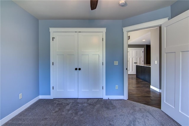unfurnished bedroom featuring baseboards, dark colored carpet, a closet, and ceiling fan