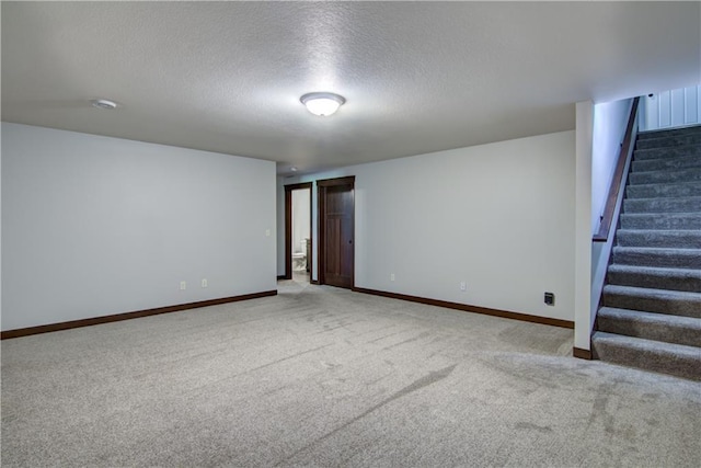 spare room featuring carpet, a textured ceiling, stairway, and baseboards