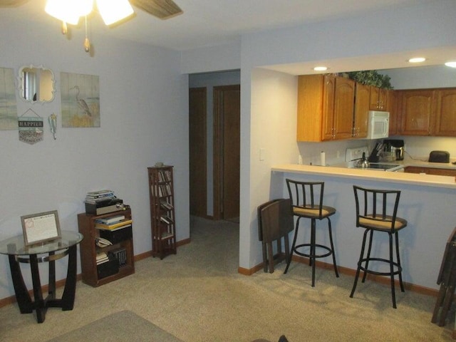 kitchen with white microwave, brown cabinetry, light countertops, a breakfast bar, and light colored carpet