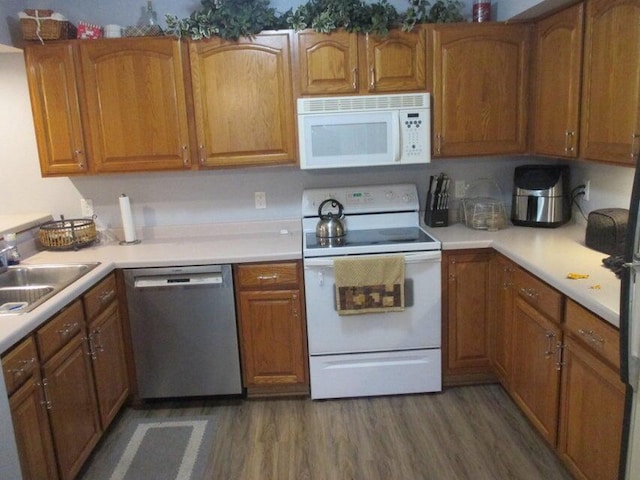 kitchen featuring white appliances, wood finished floors, a sink, and brown cabinets