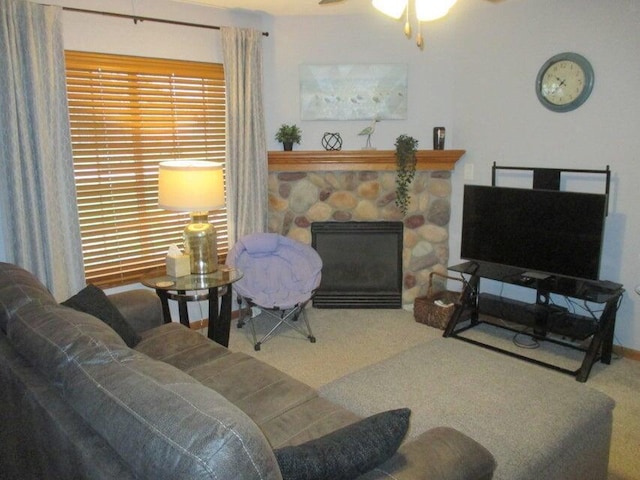 carpeted living room featuring a stone fireplace and ceiling fan