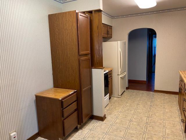 301 E Coldspring Ave, Madison, WI 53716 - kitchen with wallpapered walls, arched walkways, light flooring, freestanding refrigerator, and brown cabinetry