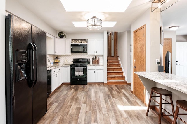 7929 N Pine View Dr, Edgerton, WI 53534 - kitchen with black appliances, a skylight, white cabinets, light stone counters, and decorative backsplash