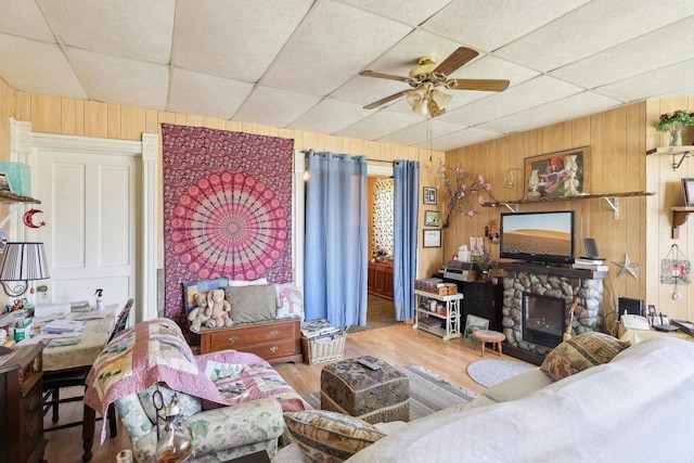 604 9th Ave, Baraboo, WI 53913 - living area with wooden walls, a stone fireplace, a drop ceiling, a ceiling fan, and wood finished floors