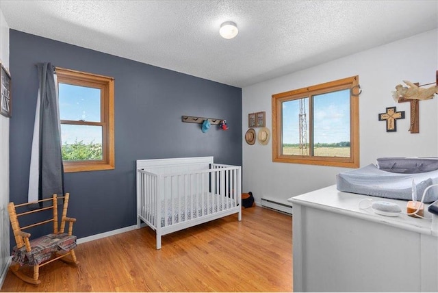 E7065 County Road B, Colfax, WI 54730 - bedroom with a baseboard heating unit, light wood-style flooring, and a textured ceiling