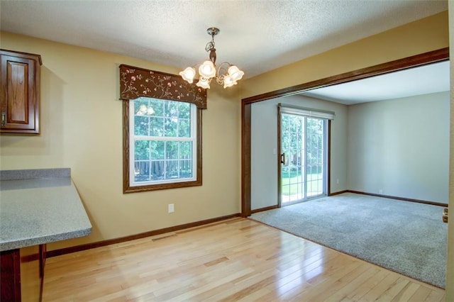 1206 Nixon Ave, Eau Claire, WI 54701 - unfurnished dining area with a chandelier, plenty of natural light, light wood-style flooring, baseboards, and a textured ceiling