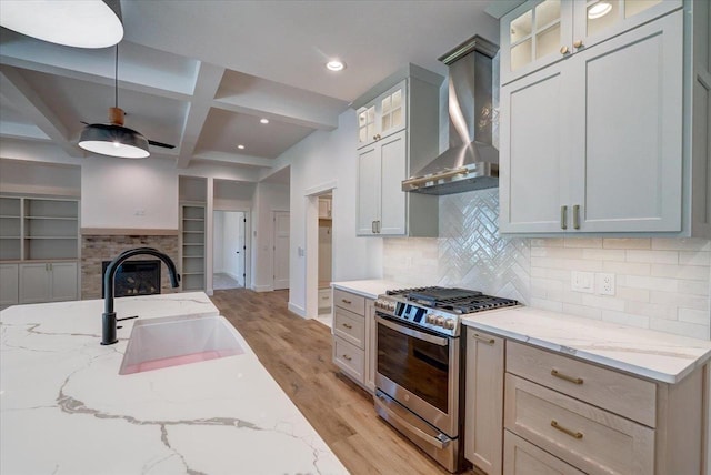 713 Kennedy St, Sauk City, WI 53583 - kitchen featuring stainless steel range with gas stovetop, a sink, wall chimney exhaust hood, light wood finished floors, and light stone counters