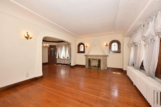 3434 N 45th St, Milwaukee, WI 53216 - unfurnished living room with radiator heating unit, arched walkways, a chandelier, hardwood / wood-style flooring, and crown molding