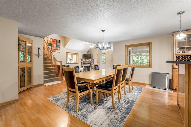 dining space featuring a fireplace, a textured ceiling, light wood-style flooring, baseboards, and stairway