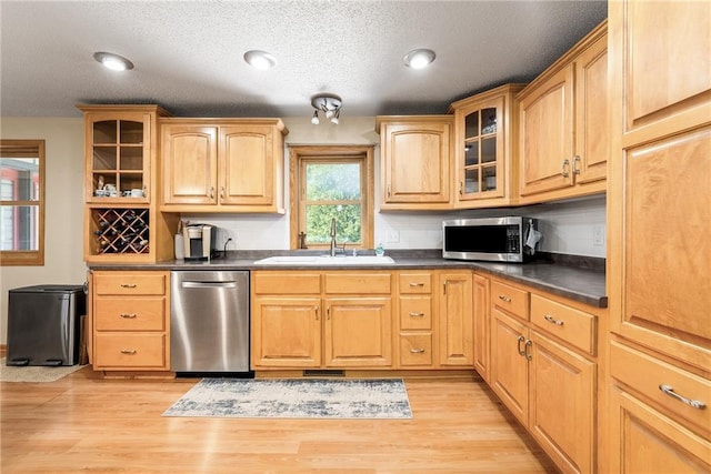 kitchen with stainless steel appliances, a sink, dark countertops, glass insert cabinets, and light wood finished floors